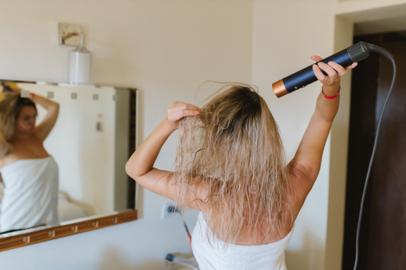 Young woman drying her hair with a styler, a hair dryer at home. 