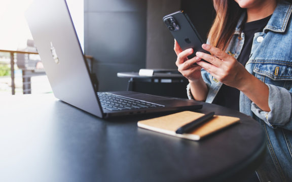 une femme utilise son iphone avec son macbook Apple