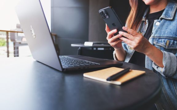 une femme utilise son iphone avec son macbook Apple