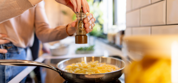Woman grinding pepper on pasta in modern kitchen