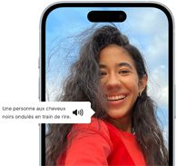 Un iPhone 15 affichant une annonce VoiceOver décrivant le contenu d’une photographie en ces termes : une personne aux cheveux noirs ondulés en train de rire