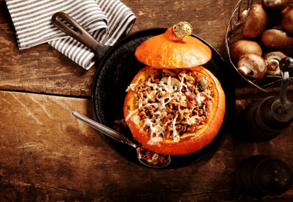 Tasty autumn stuffed pumpkin with fresh mushrooms ready to serve for a seasonal dinner, overhead view on rustic wooden table with copyspace