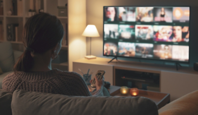 Woman relaxing on the couch, she is using the remote control and choosing a TV show or movie on the television menu